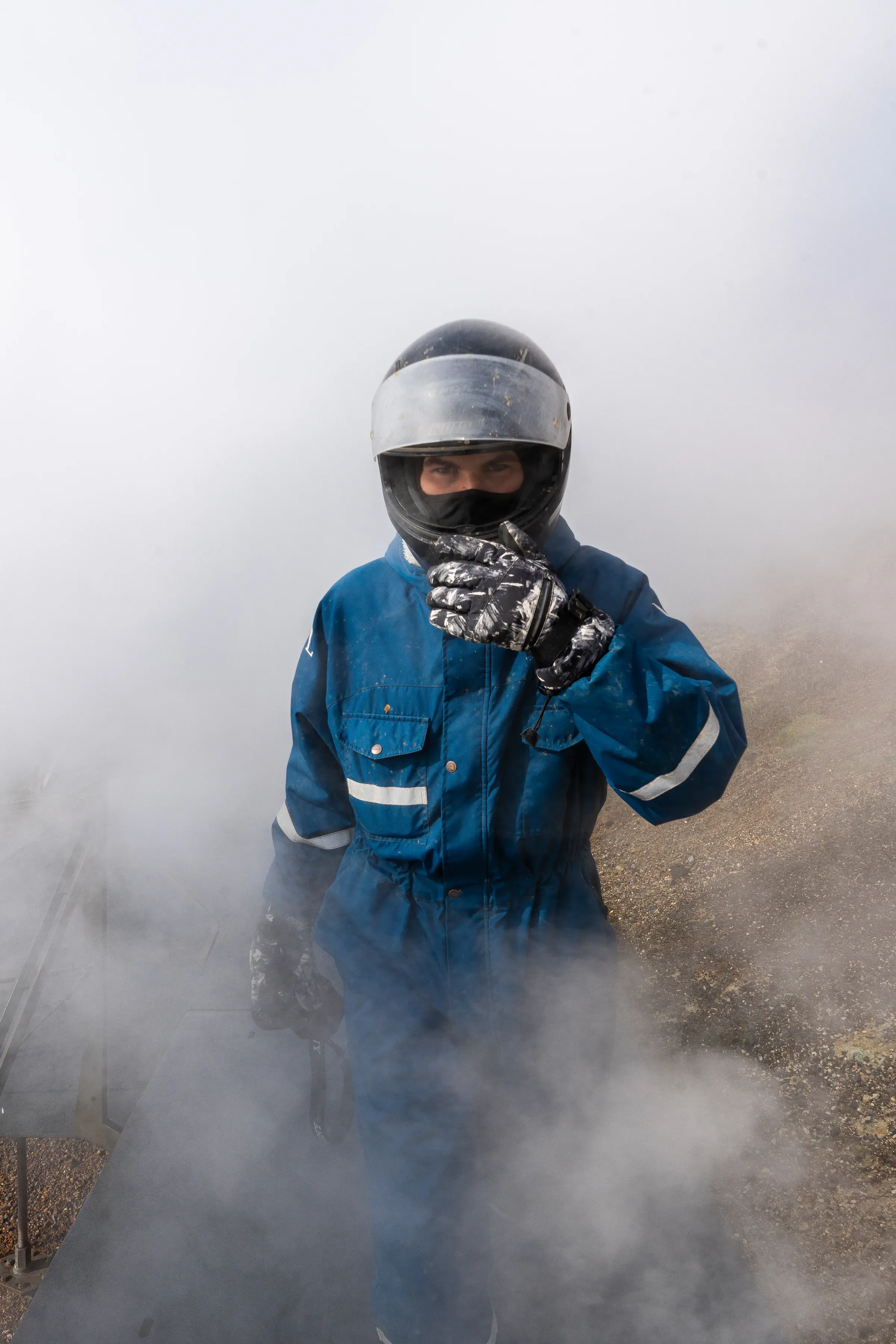 Rider in a helmet and blue overalls surrounded by geothermal steam