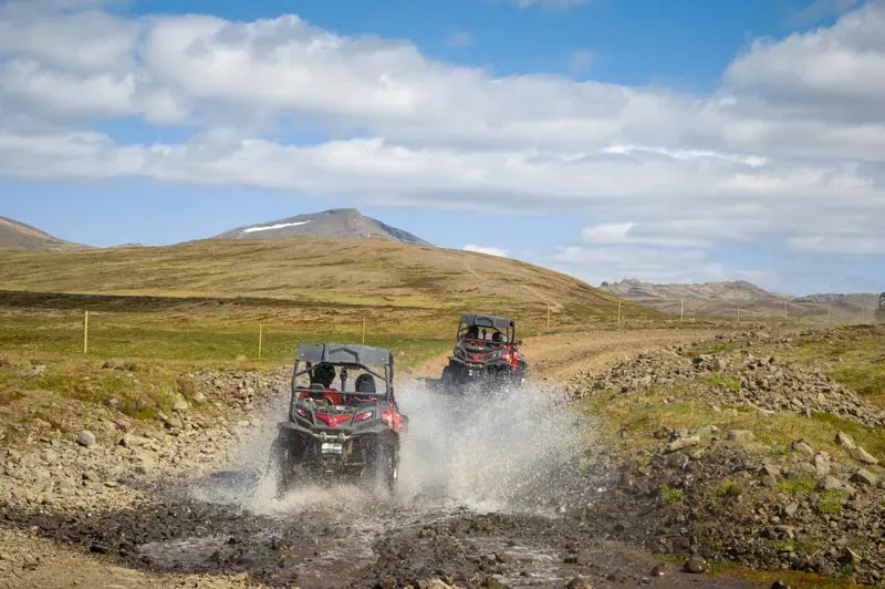 Two buggies throwing up spray as they drive through a puddle