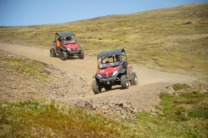 Two buggies climbing a dusty track across a grassy hillside