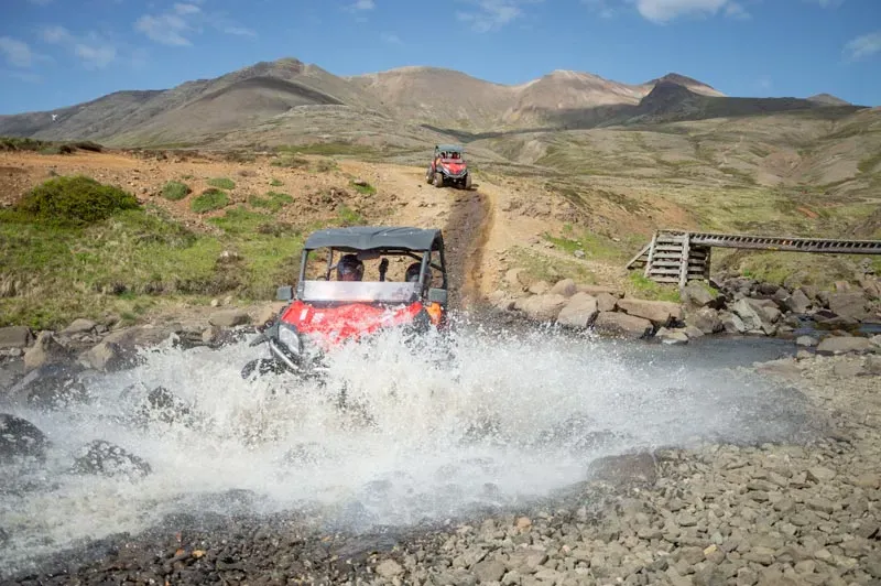 Buggy splashing through a stream below a wooden footbridge