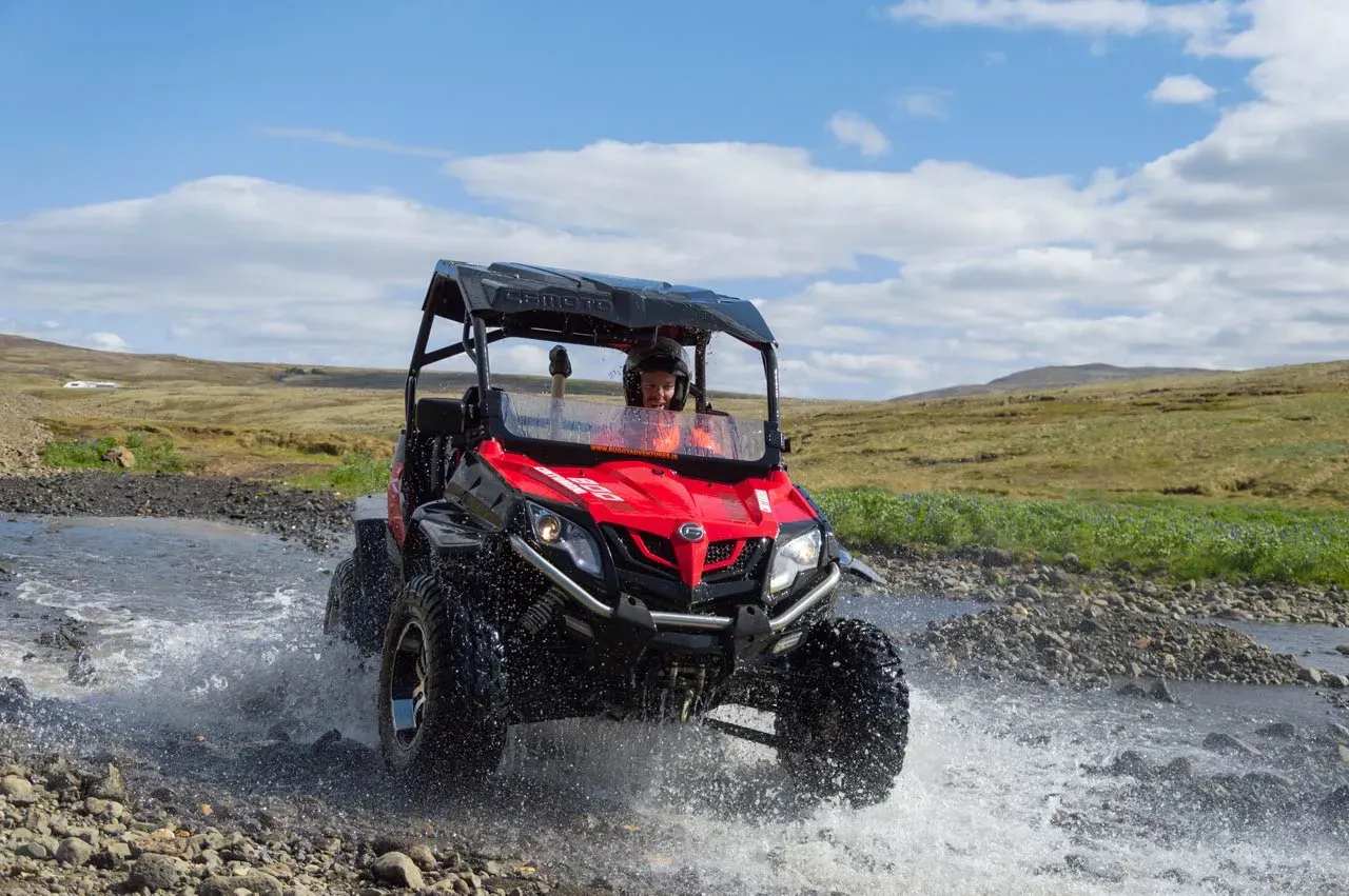 Red buggy splashing through a shallow river under a blue sky