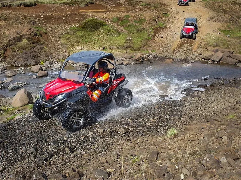 Red buggy driving through a stream on a rocky mountain track