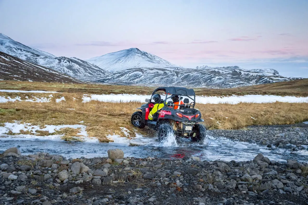 Buggy crossing a river below snow-covered mountains