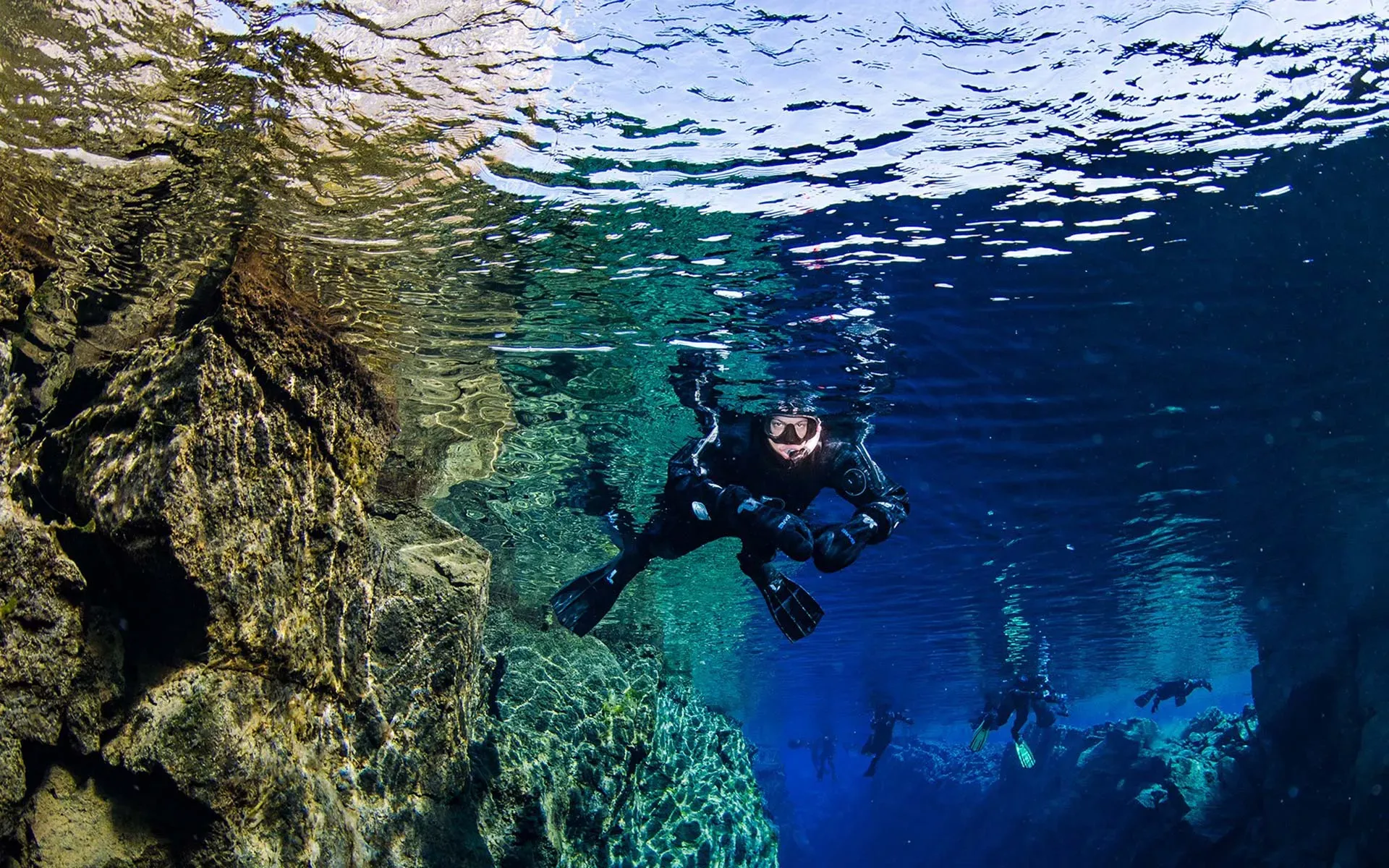 Snorkeller swimming beside the rock wall of the Silfra fissure