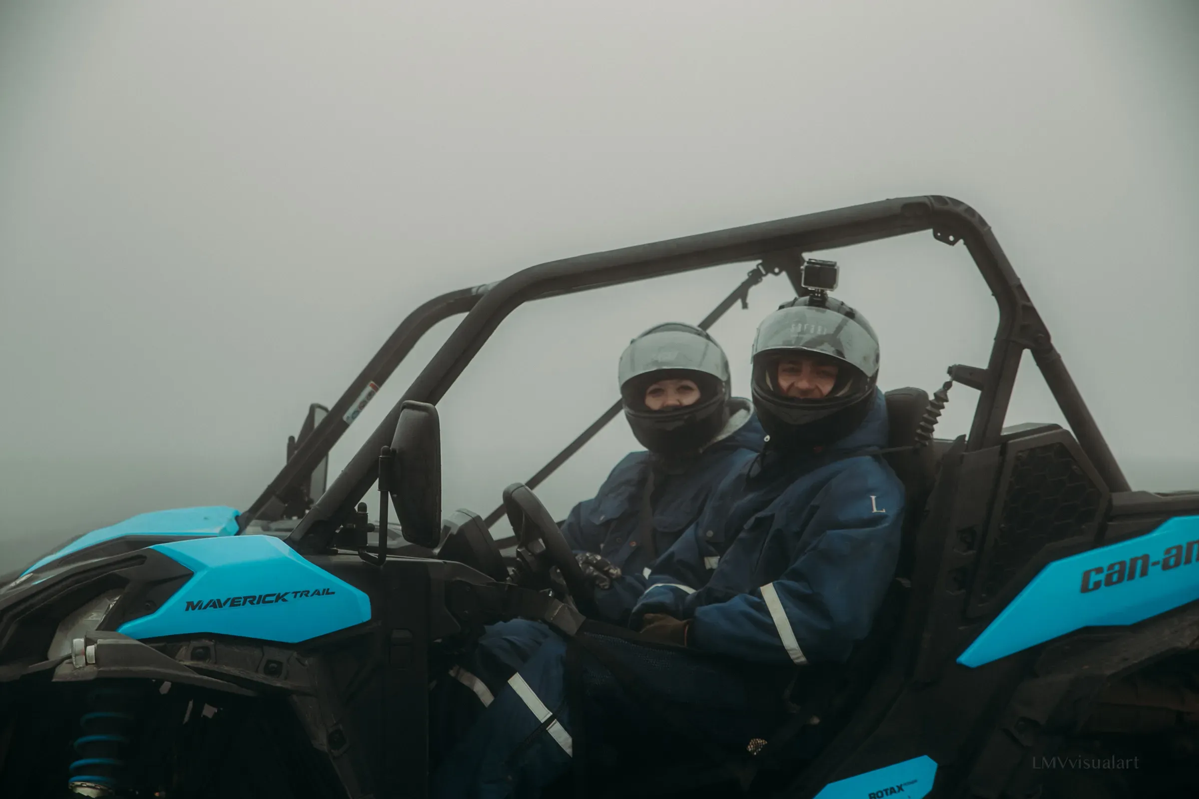 Two riders in helmets seated in a blue Can-Am buggy