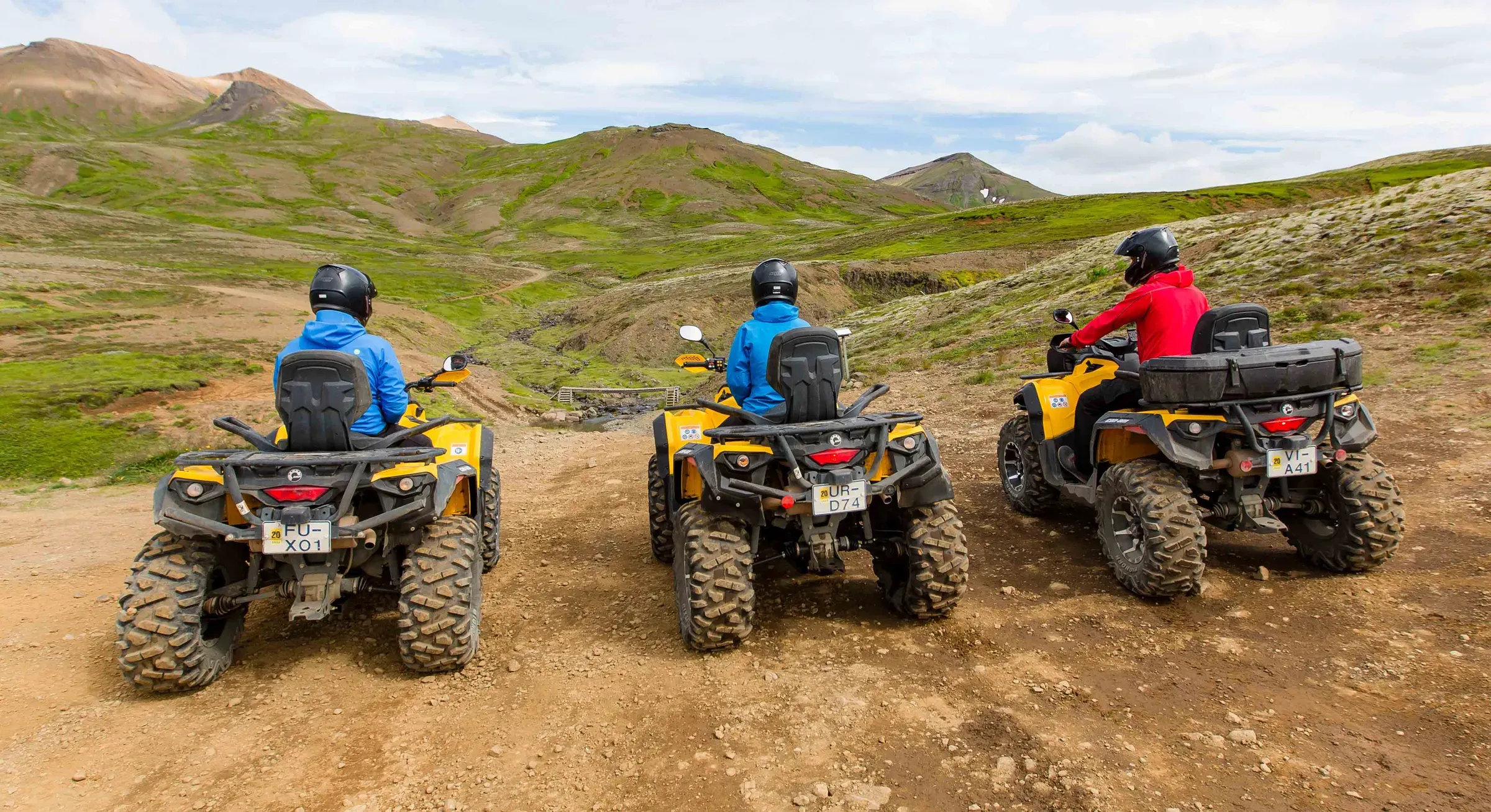 Three riders on yellow ATVs on a gravel track