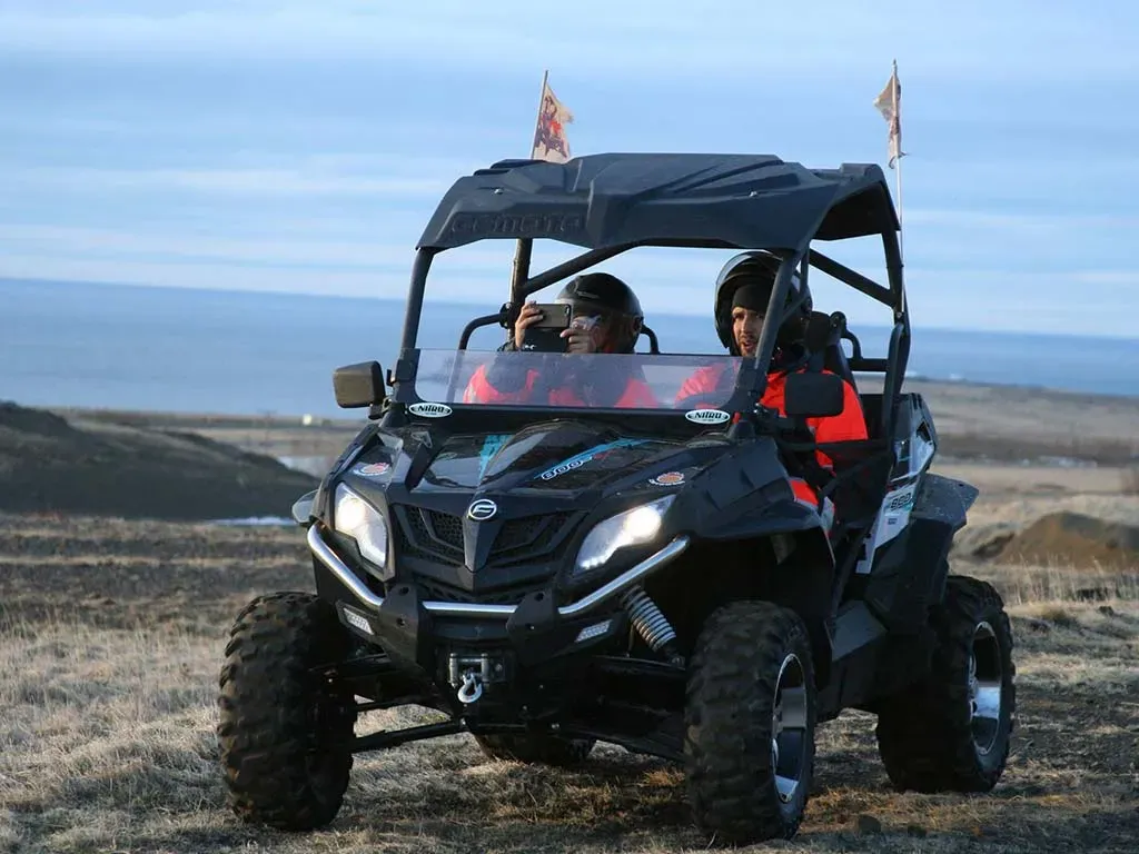 Two riders in a black buggy on a coastal track